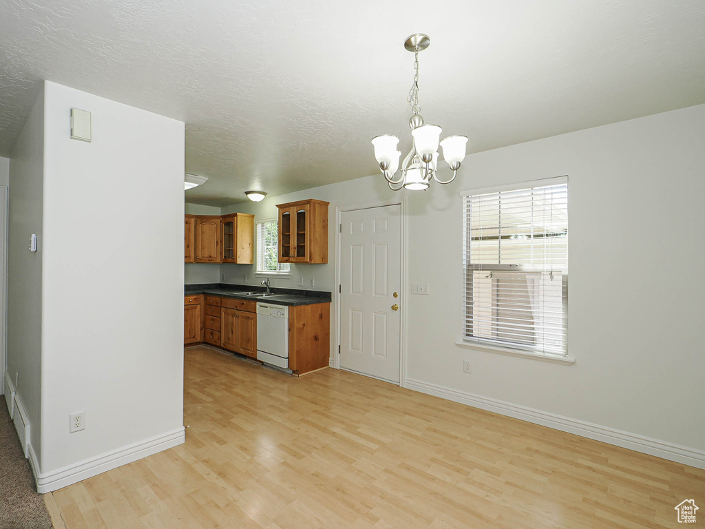 Kitchen with dishwasher, brown cabinets, dark countertops, light wood-style floors, and a chandelier