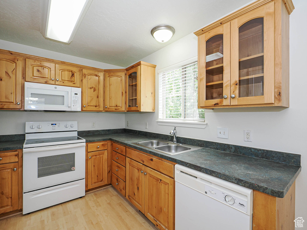 Kitchen featuring white appliances, light wood finished floors, dark countertops, glass insert cabinets, and brown cabinets