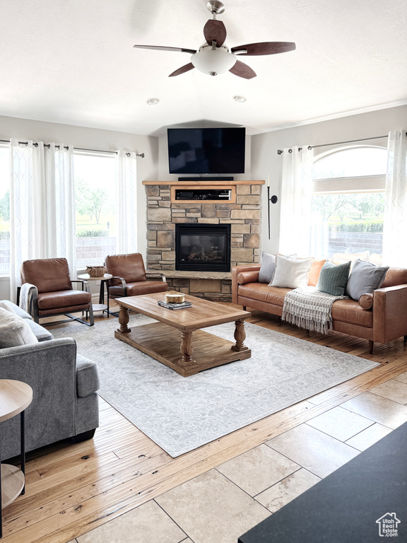 Living area with a ceiling fan, light wood-style flooring, and a stone fireplace