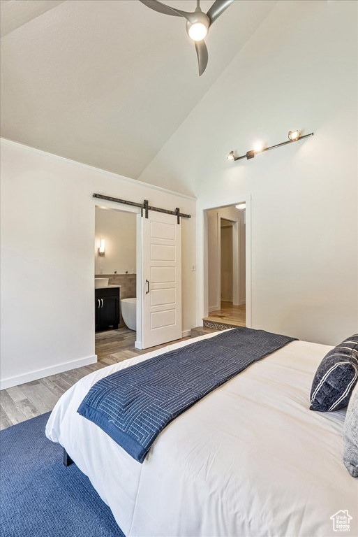 Bedroom with a barn door, wood finished floors, connected bathroom, high vaulted ceiling, and a ceiling fan