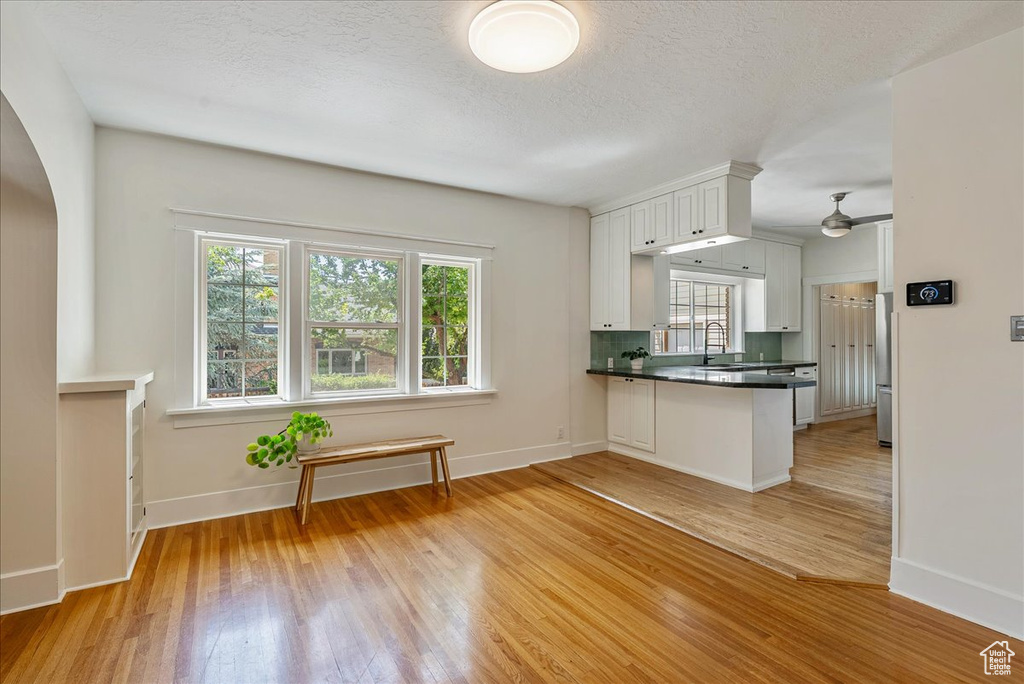 Kitchen with stainless steel fridge, light wood-style floors, white cabinets, arched walkways, and a peninsula