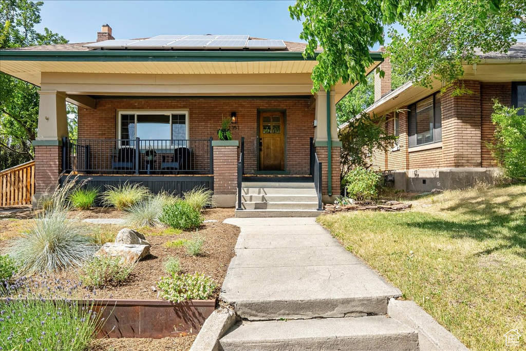 View of front of house featuring a porch, brick siding, solar panels, and a chimney