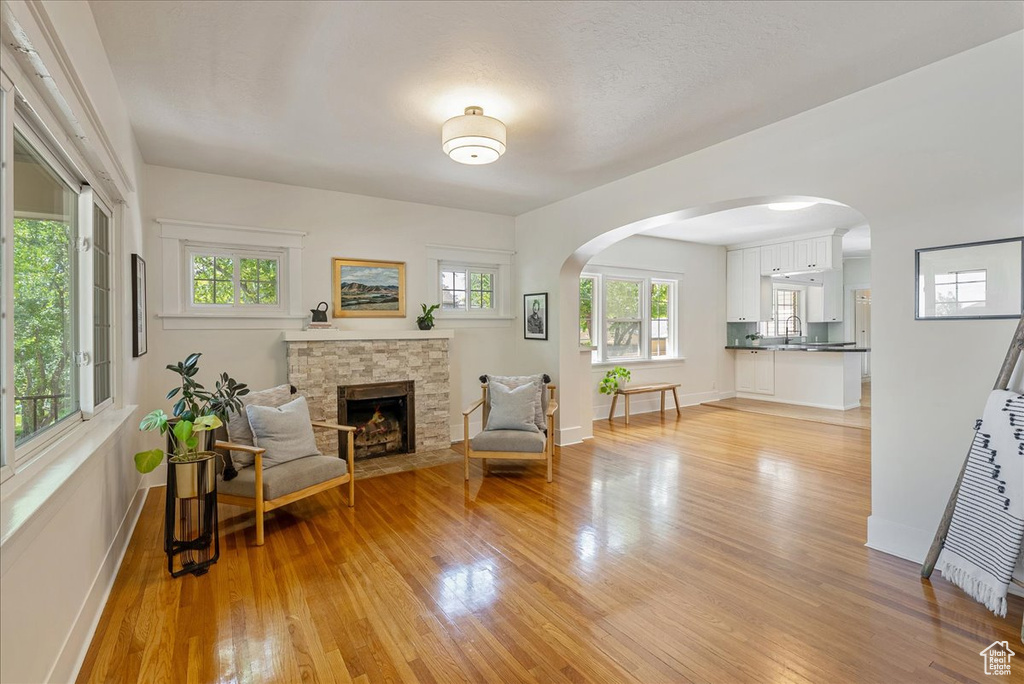 Living area featuring light wood finished floors, a stone fireplace, and arched walkways