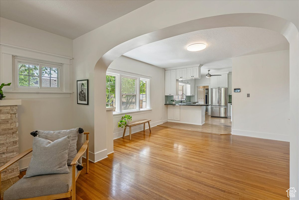 Living area featuring arched walkways, plenty of natural light, light wood-type flooring, and ceiling fan