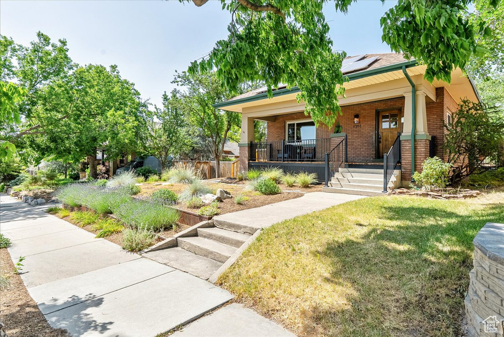 View of front facade with brick siding, a porch, roof mounted solar panels, and a front yard
