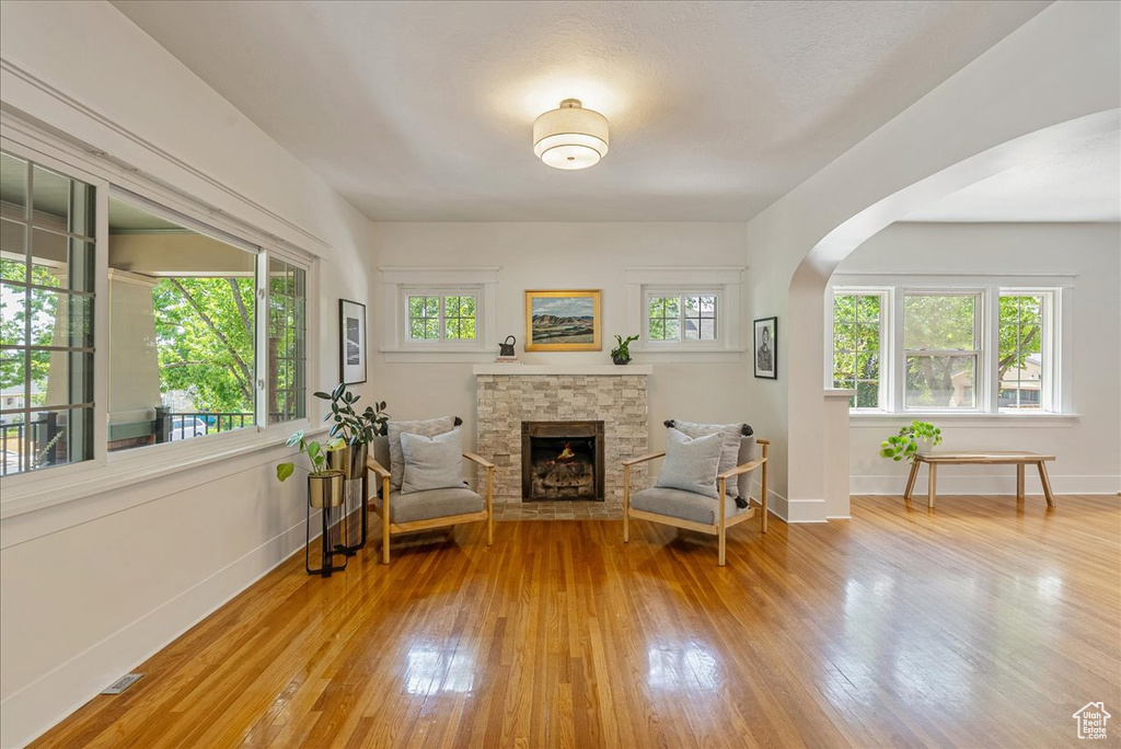 Sitting room with light wood finished floors, arched walkways, and a stone fireplace