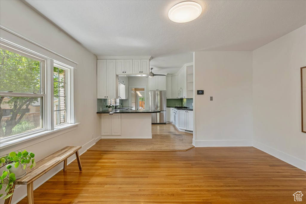 Kitchen with freestanding refrigerator, dark countertops, light wood-type flooring, white cabinets, and a peninsula