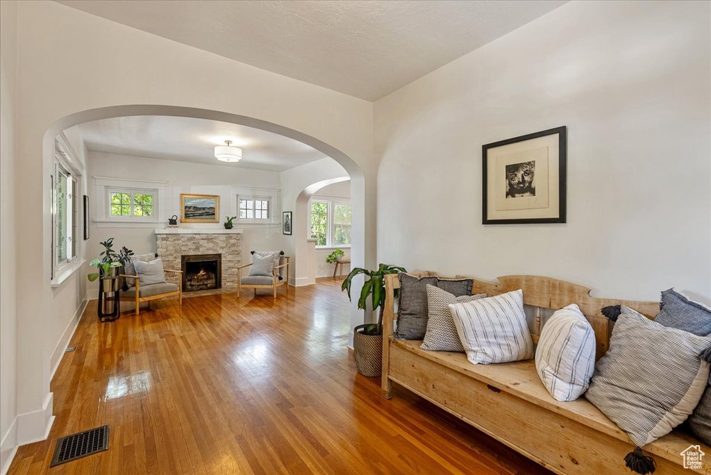 Living room with wood finished floors, a stone fireplace, and arched walkways