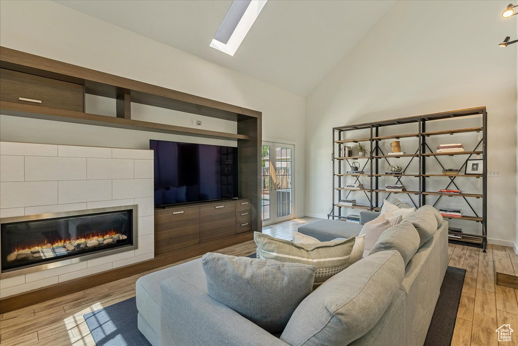Living room with a tiled fireplace, high vaulted ceiling, light wood finished floors, and a skylight