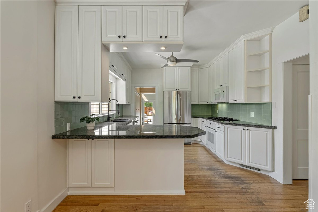 Kitchen featuring open shelves, white appliances, a peninsula, light wood-style flooring, and decorative backsplash