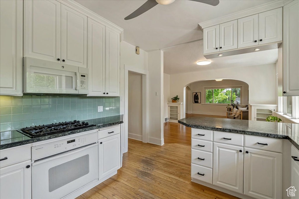 Kitchen with white appliances, arched walkways, a ceiling fan, white cabinets, and backsplash
