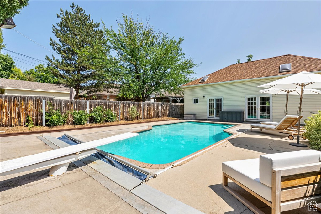 View of swimming pool with a patio area, a diving board, a fenced backyard, and french doors