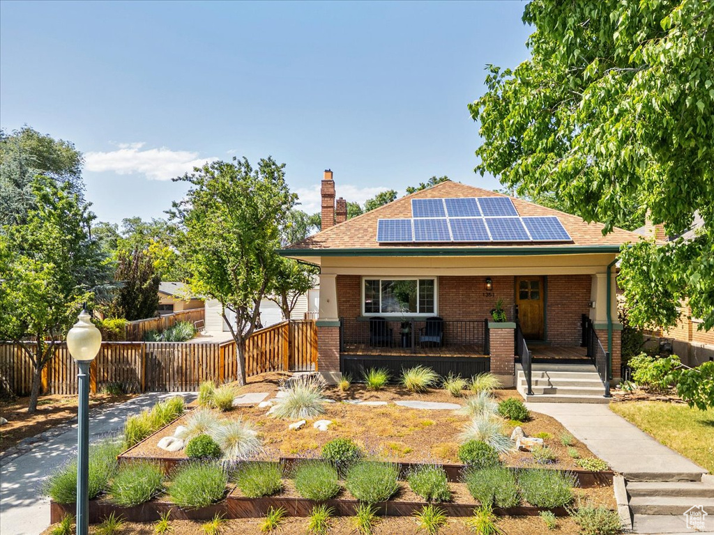 Bungalow-style home featuring a chimney, a porch, solar panels, brick siding, and roof with shingles