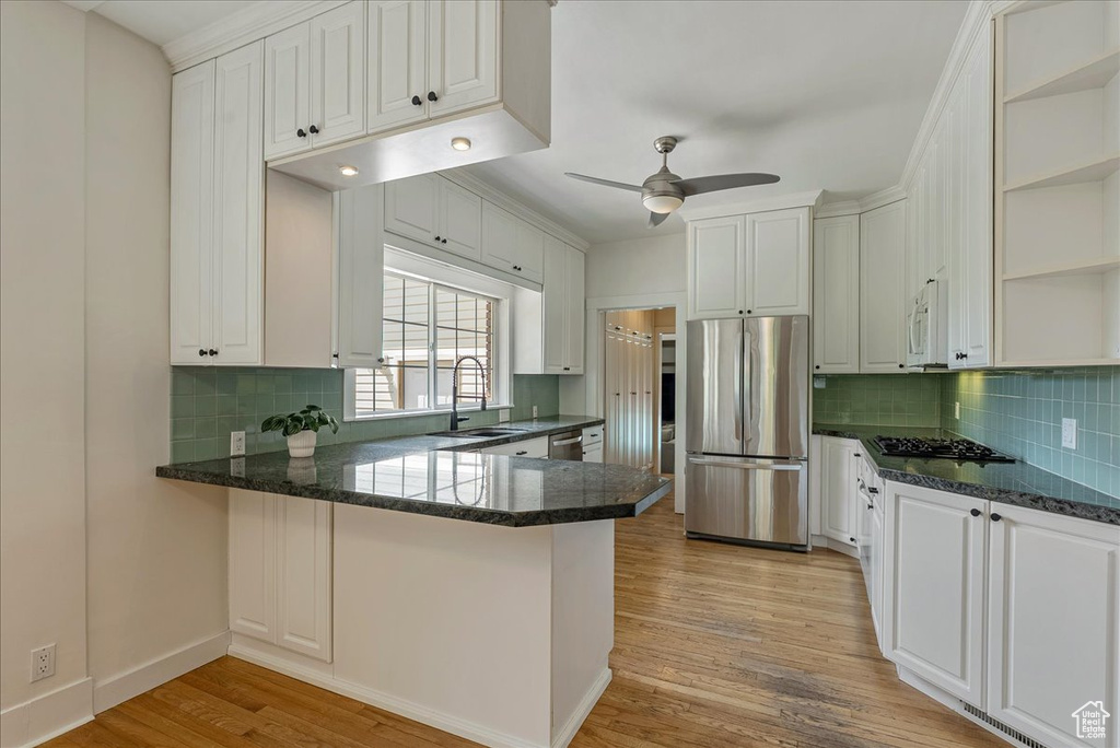 Kitchen featuring appliances with stainless steel finishes, open shelves, a peninsula, light wood-style flooring, and tasteful backsplash