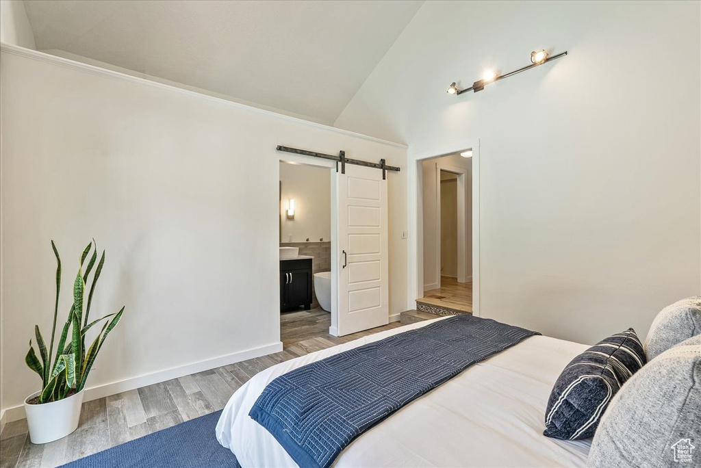 Bedroom featuring a barn door, wood finished floors, connected bathroom, and high vaulted ceiling