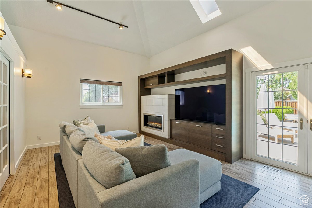 Living area with track lighting, a skylight, high vaulted ceiling, light wood-style flooring, and a tile fireplace