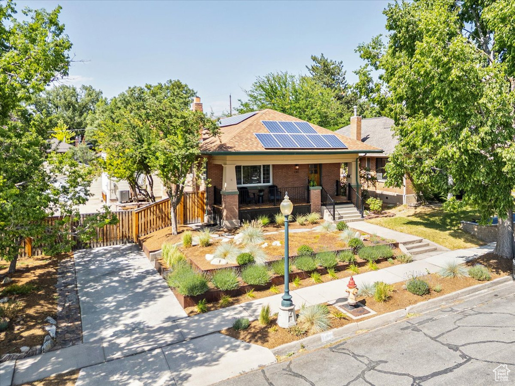 View of front of house featuring a porch, solar panels, brick siding, a chimney, and a shingled roof