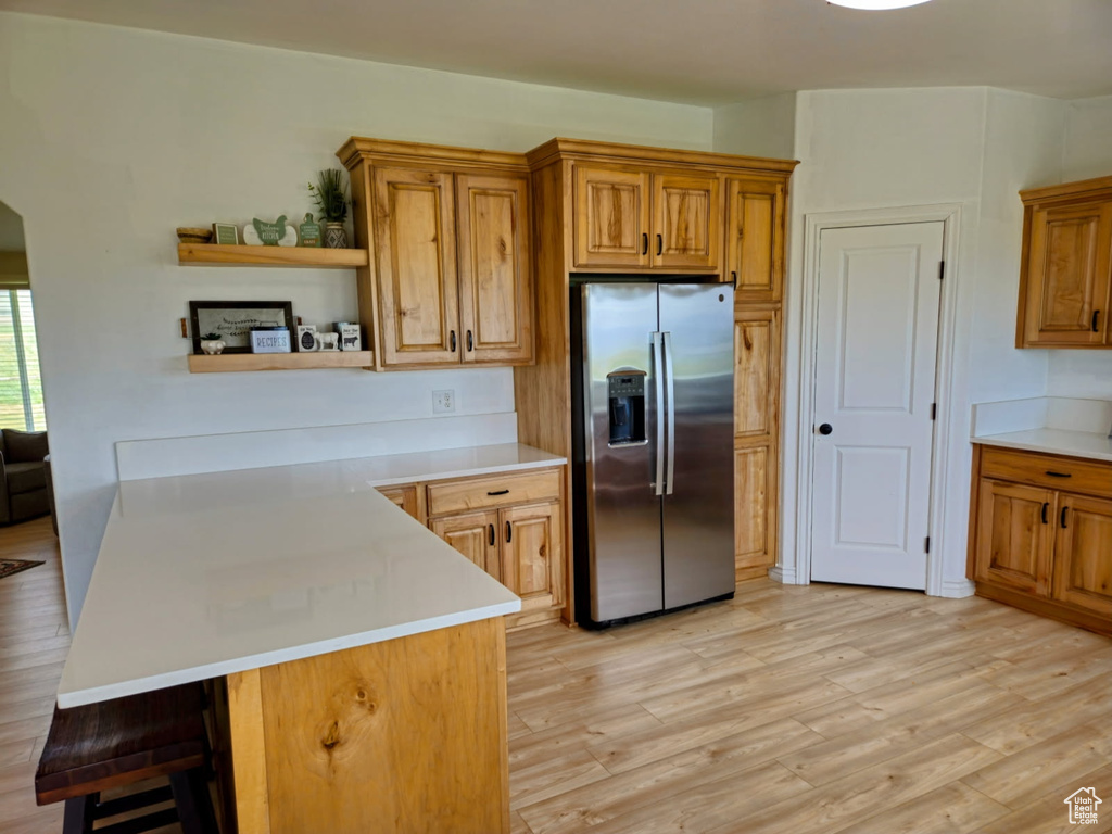 Kitchen with stainless steel refrigerator with ice dispenser, open shelves, a peninsula, light countertops, and a kitchen bar