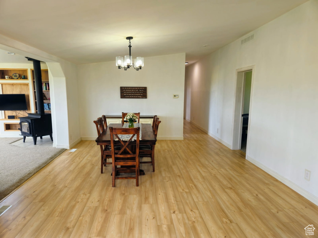 Dining area with a wood stove, light wood finished floors, and a chandelier