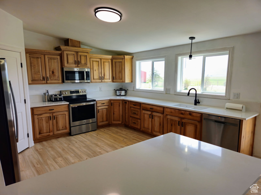 Kitchen with stainless steel appliances, brown cabinets, light wood-type flooring, light countertops, and vaulted ceiling
