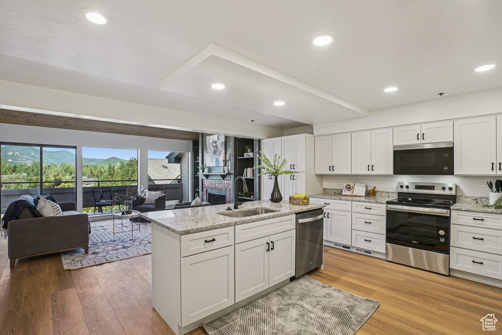 Kitchen featuring stainless steel appliances, open floor plan, white cabinetry, a center island with sink, and light wood-style flooring