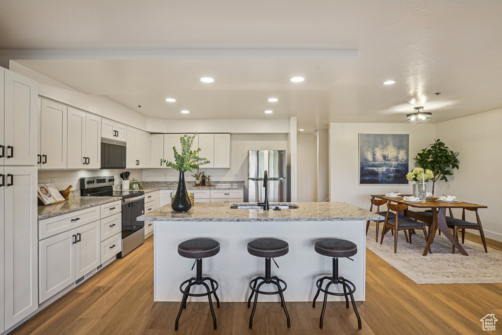 Kitchen with stainless steel appliances, a breakfast bar, an island with sink, light wood-style floors, and recessed lighting