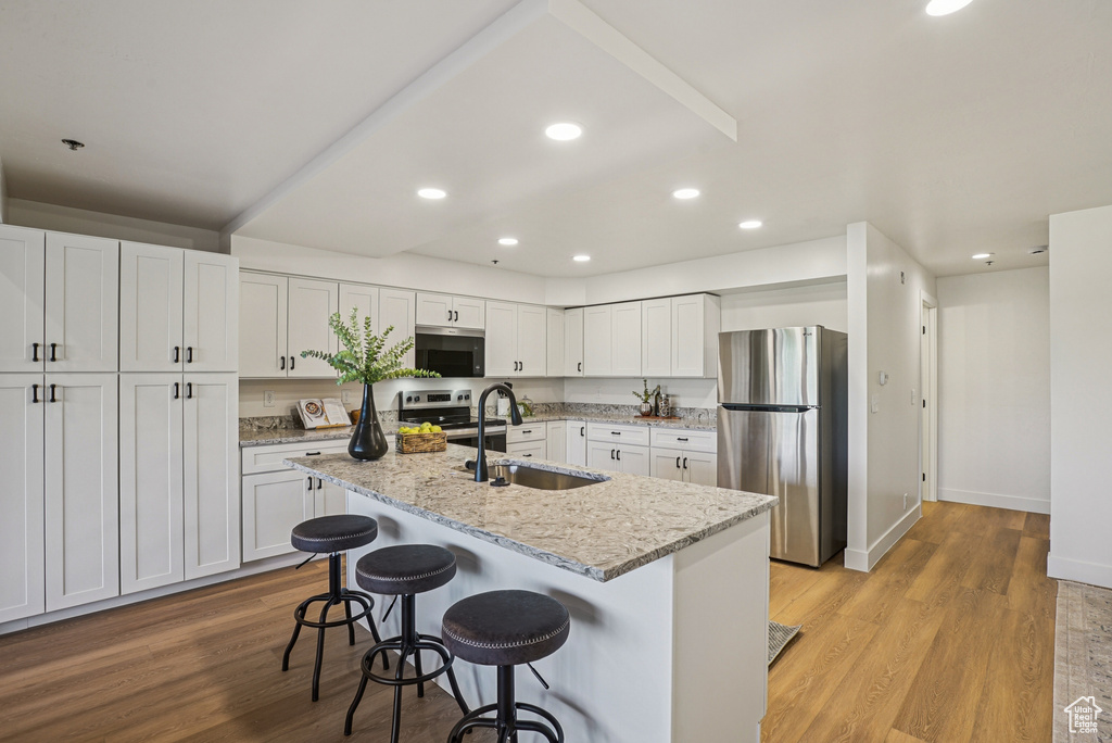 Kitchen featuring stainless steel appliances, white cabinetry, light wood-style flooring, a breakfast bar area, and recessed lighting
