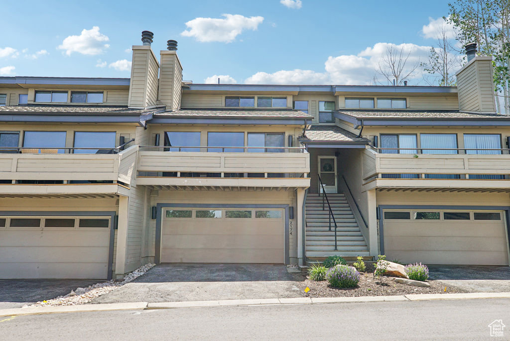 View of property with a chimney, a balcony, and driveway