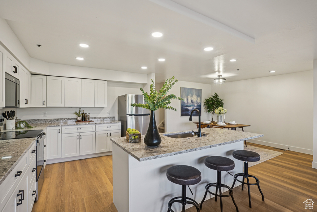 Kitchen with stainless steel appliances, a breakfast bar, white cabinets, light wood finished floors, and light stone counters
