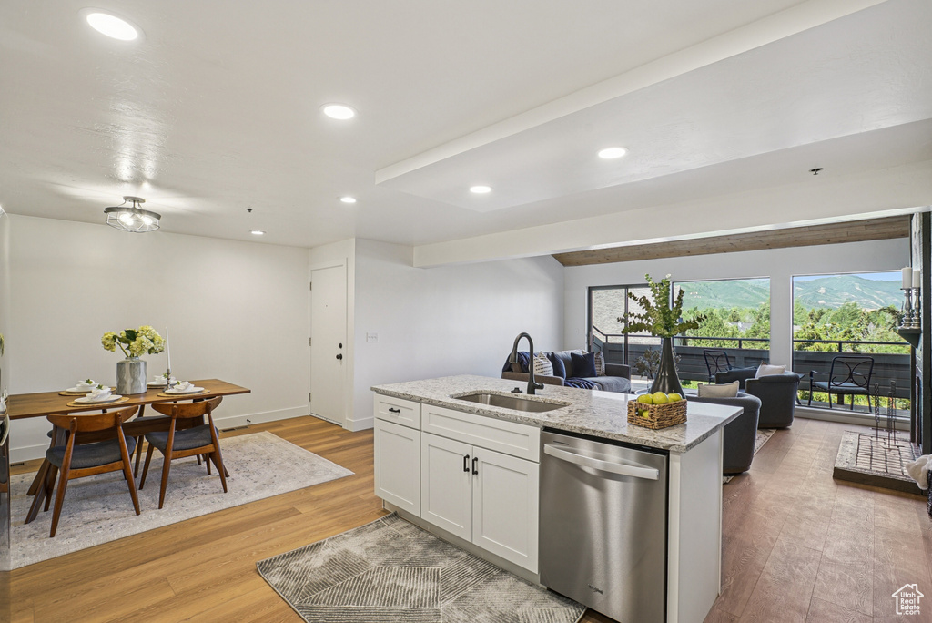 Kitchen with stainless steel dishwasher, open floor plan, light wood-style flooring, a kitchen island with sink, and light stone counters