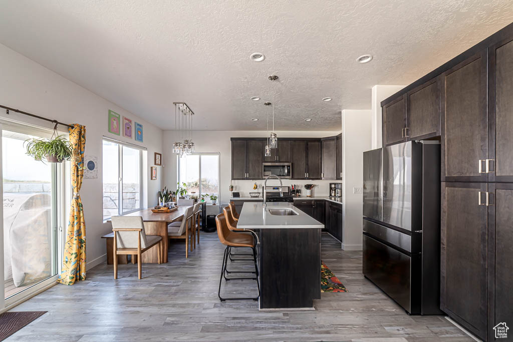 Kitchen with appliances with stainless steel finishes, dark brown cabinetry, light countertops, a textured ceiling, and light wood-style floors