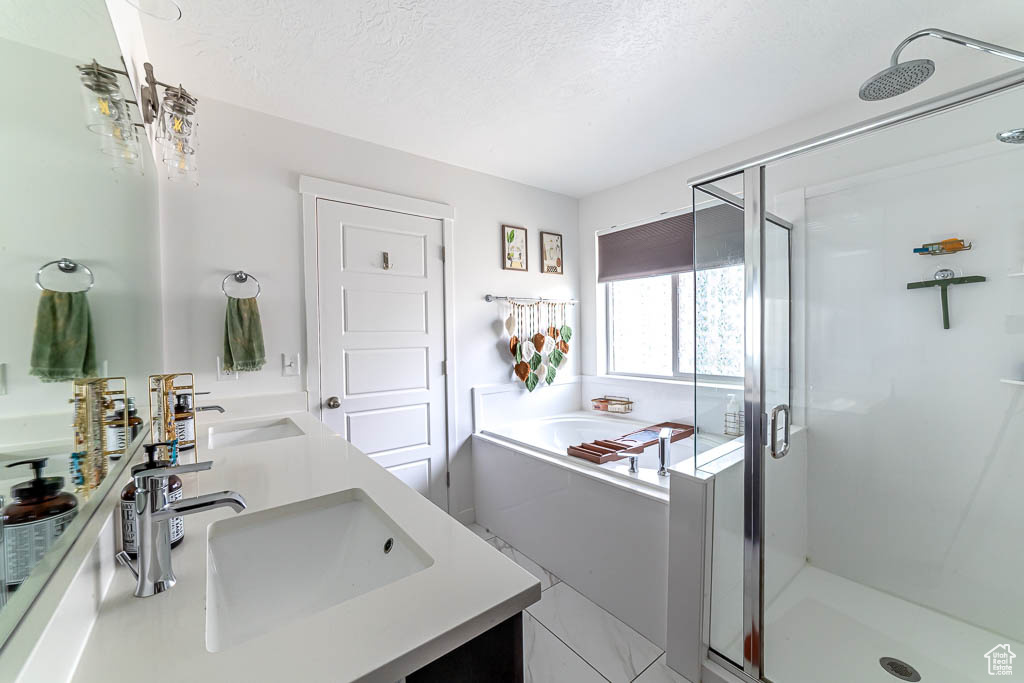 Full bathroom featuring double vanity, a stall shower, a bath, and a textured ceiling