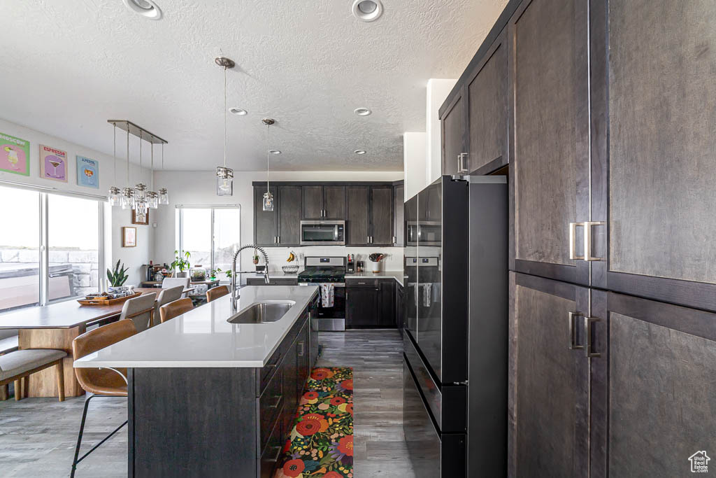 Kitchen featuring appliances with stainless steel finishes, a kitchen breakfast bar, dark brown cabinetry, a textured ceiling, and an island with sink