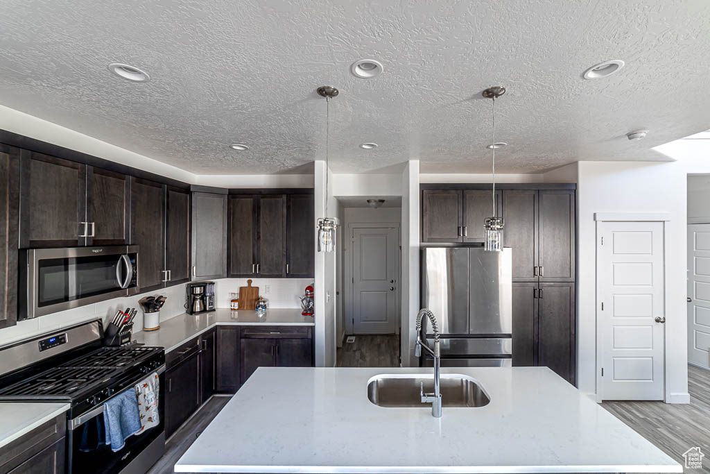 Kitchen with appliances with stainless steel finishes, a textured ceiling, dark brown cabinets, light countertops, and a center island with sink