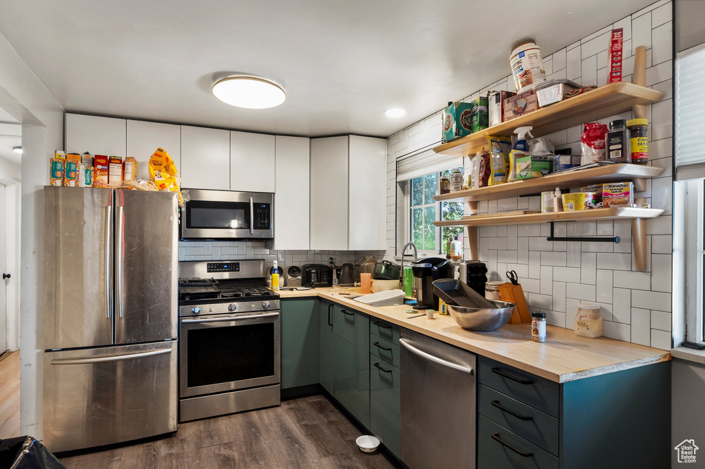 Kitchen with appliances with stainless steel finishes, dark wood-type flooring, tasteful backsplash, open shelves, and light countertops