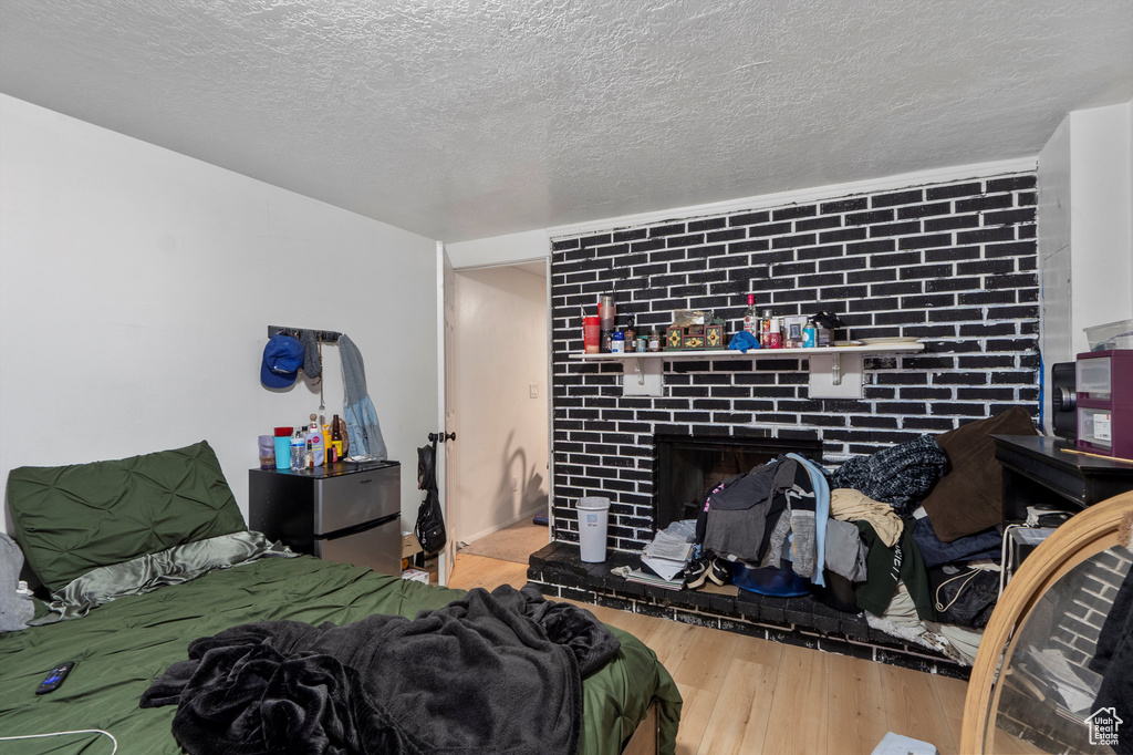 Bedroom with wood finished floors, a brick fireplace, and a textured ceiling