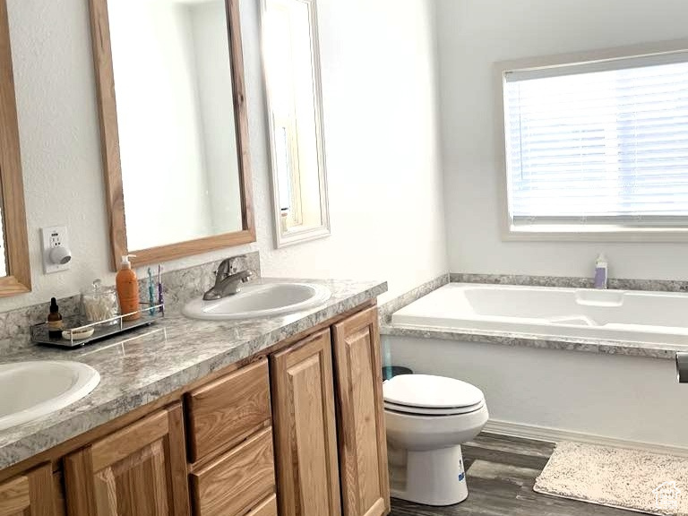 Full bath featuring double vanity, a garden tub, and wood finished floors