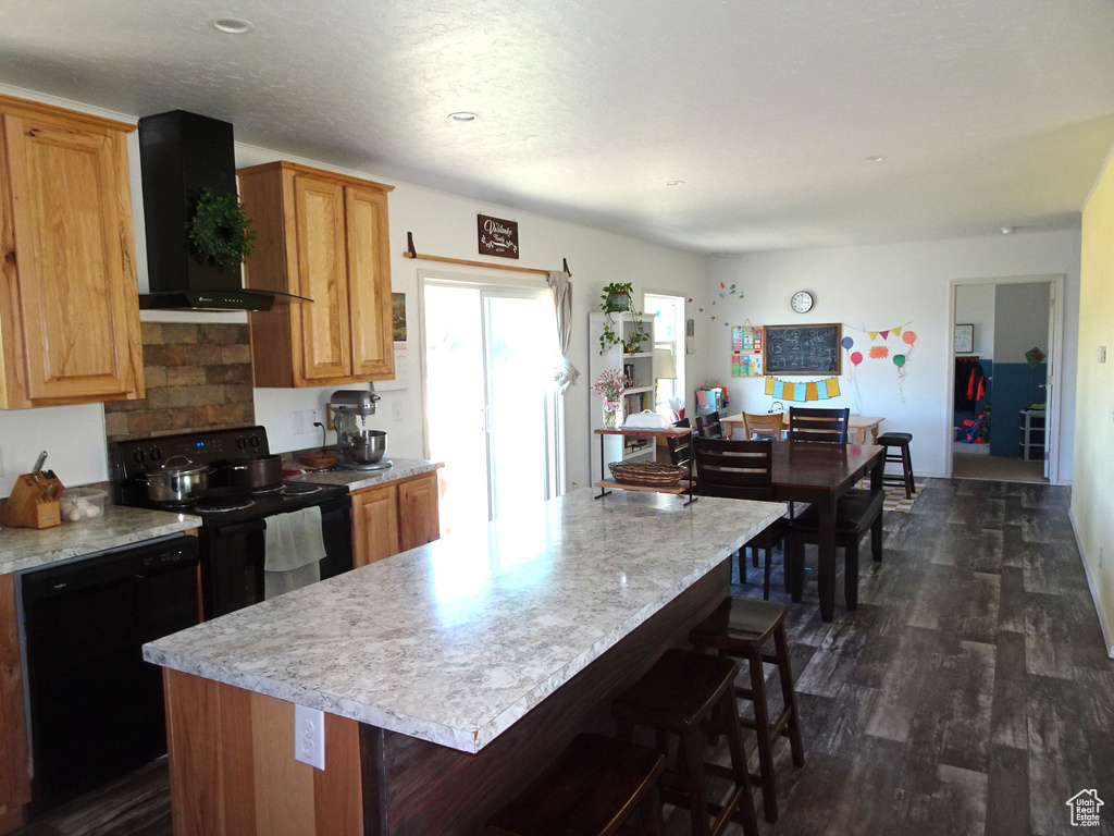 Kitchen with wall chimney exhaust hood, black appliances, light countertops, and dark wood-style flooring