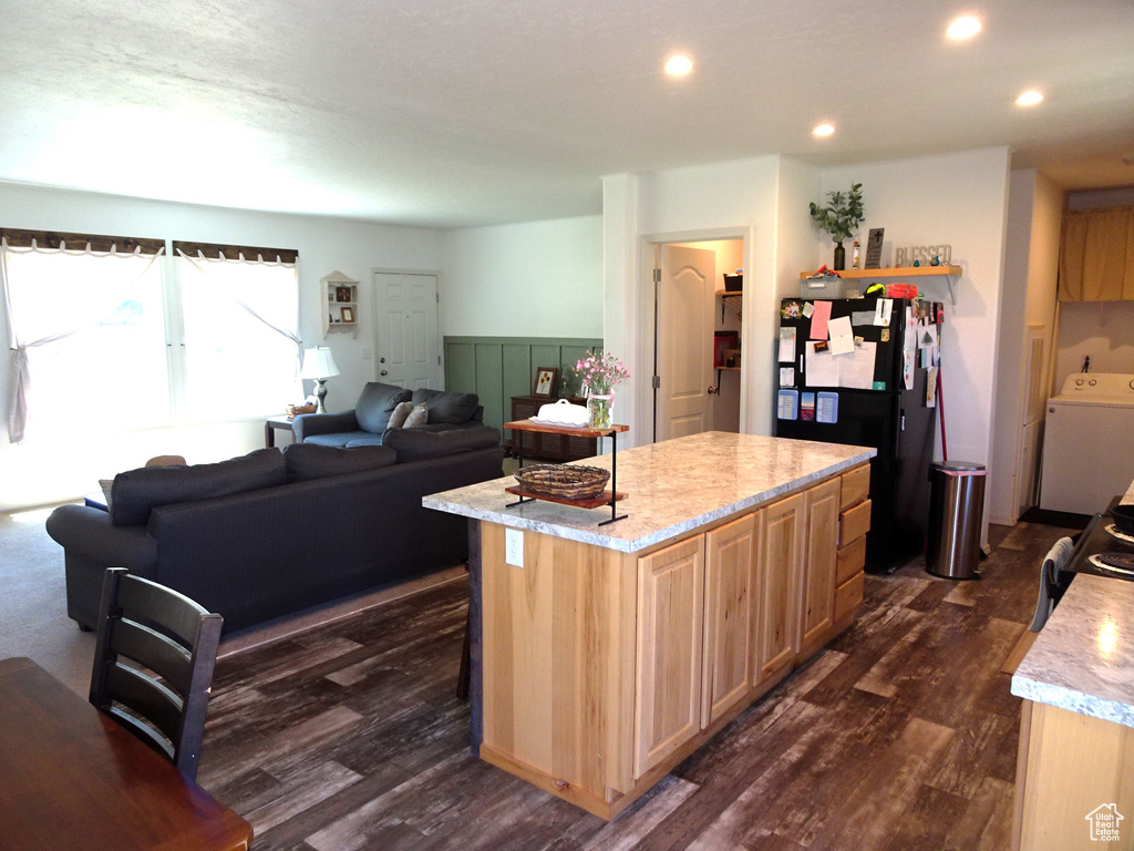 Kitchen featuring washer / dryer, black appliances, dark wood-style floors, a kitchen island, and light stone countertops