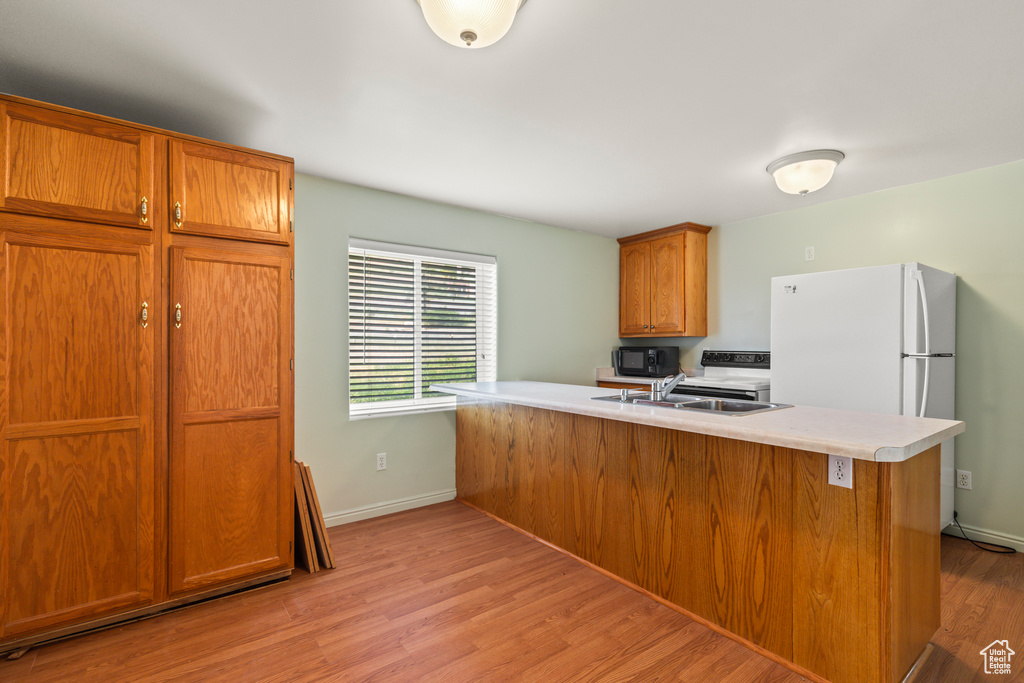 Kitchen with light wood-style floors, light countertops, brown cabinetry, and black microwave