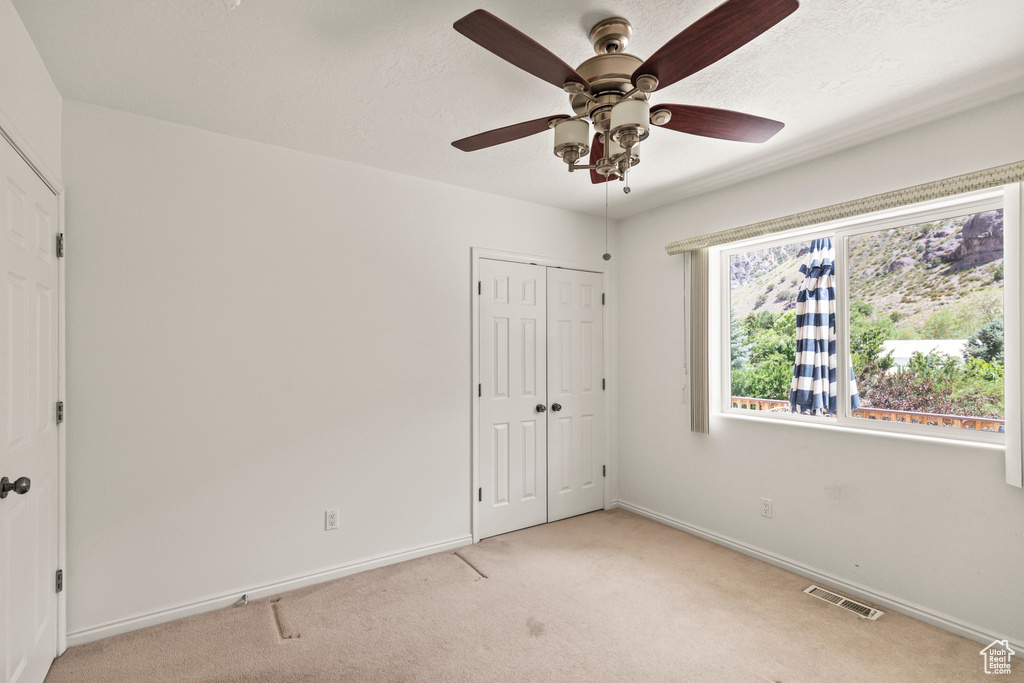 Unfurnished bedroom with light colored carpet, a closet, and ceiling fan