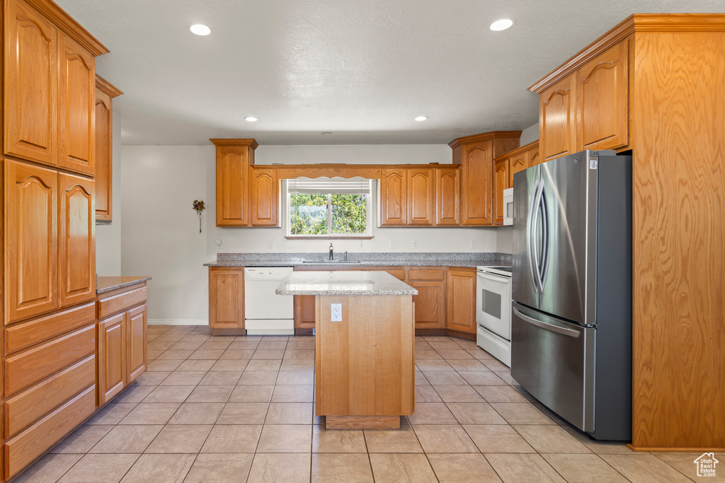 Kitchen featuring white appliances, a center island, light tile patterned flooring, recessed lighting, and brown cabinetry