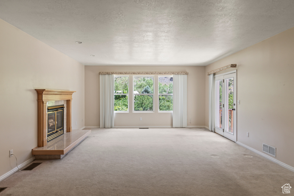 Unfurnished living room featuring carpet, a premium fireplace, and a textured ceiling