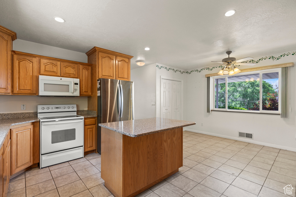 Kitchen with white appliances, light tile patterned flooring, a kitchen island, a ceiling fan, and light stone countertops