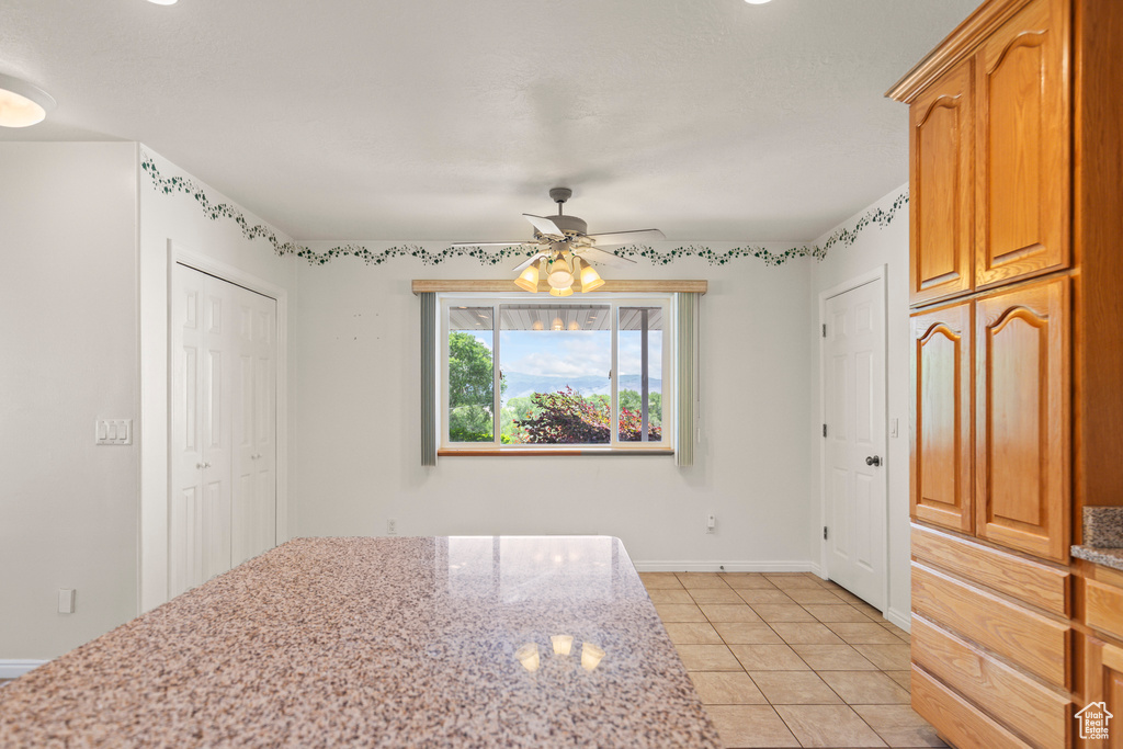 Kitchen with a ceiling fan, light stone counters, and light tile patterned flooring