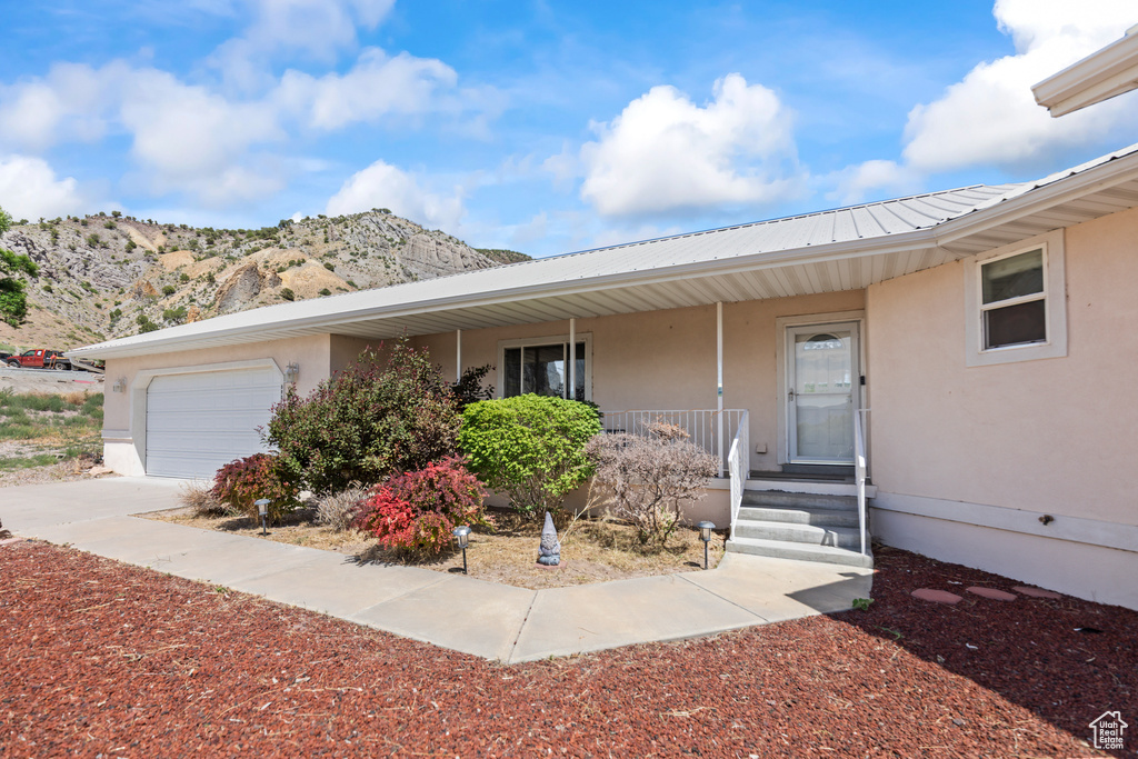 View of front of house featuring stucco siding, a porch, a mountain view, a metal roof, and an attached garage