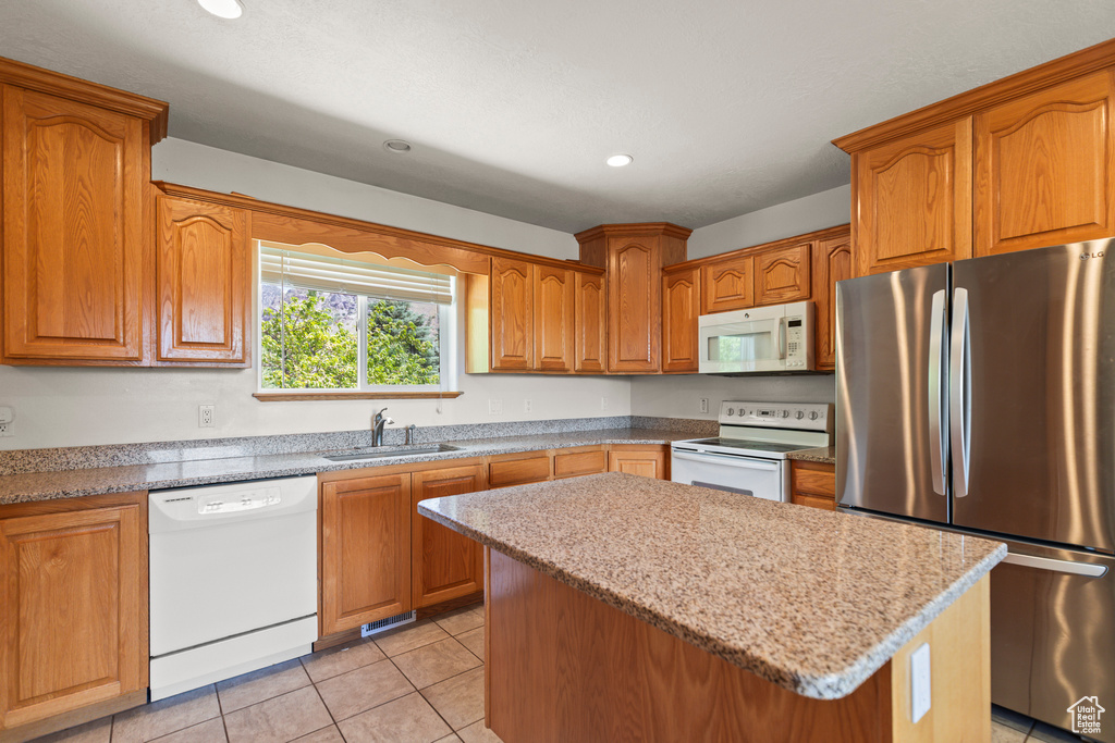 Kitchen featuring white appliances, a kitchen island, recessed lighting, light tile patterned floors, and brown cabinets
