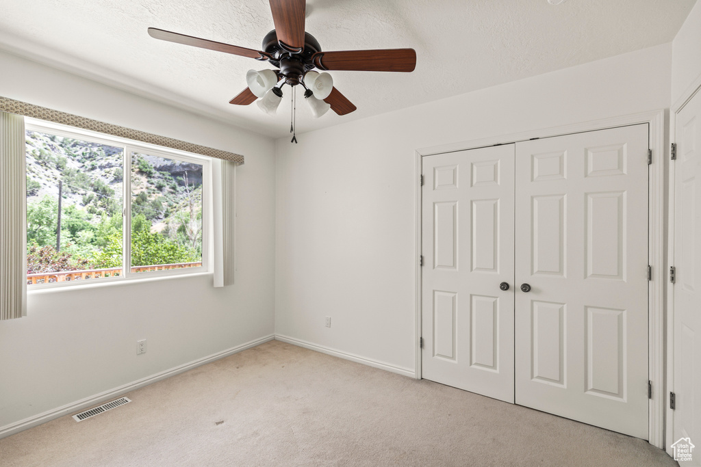 Unfurnished bedroom featuring light colored carpet, a closet, and a ceiling fan