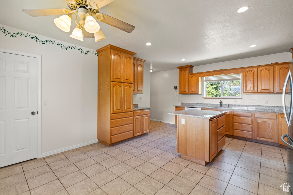 Kitchen with recessed lighting, a kitchen island, light tile patterned floors, light stone counters, and brown cabinets
