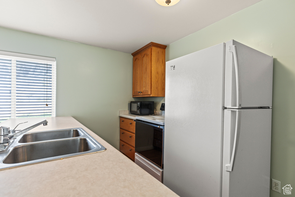 Kitchen with freestanding refrigerator, black microwave, electric range oven, light countertops, and brown cabinets